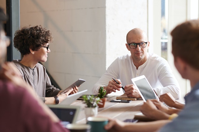 four people sitting around a table during a meeting as they all look at their iPads and take notes